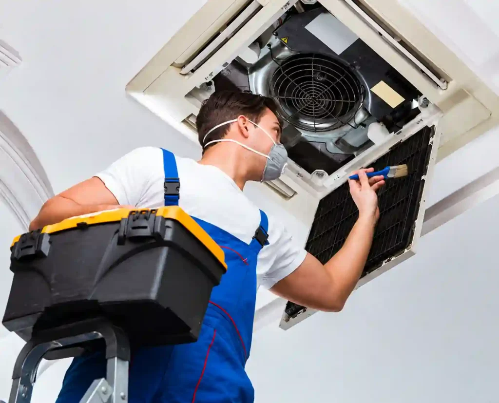 Technician cleaning an open ceiling mounted air conditioning unit.